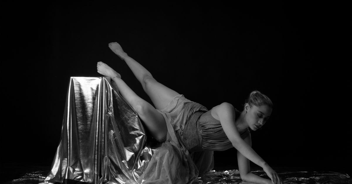 Bailarina joven ensayando una postura de danza contemporánea en un escenario con luz cálida