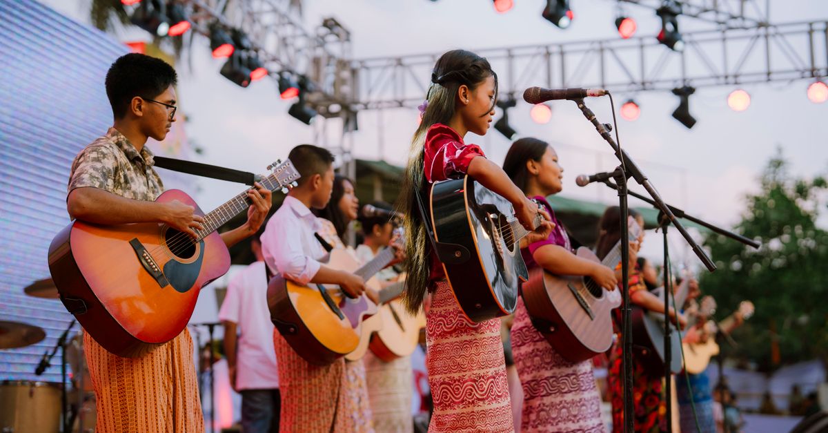 Jóvenes músicos y acróbatas compartiendo un escenario durante un ensayo con luces de sala